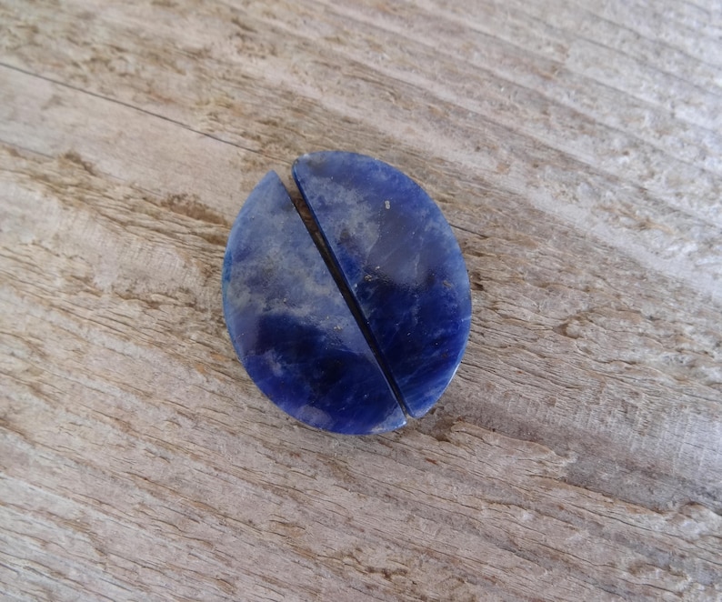 K&ouml;nnte beinhalten: Zwei H&auml;lften eines blauen Lapislazuli-Steins, jede in Form eines Halbkreises, liegen nebeneinander auf einer Holzoberfl&auml;che.
