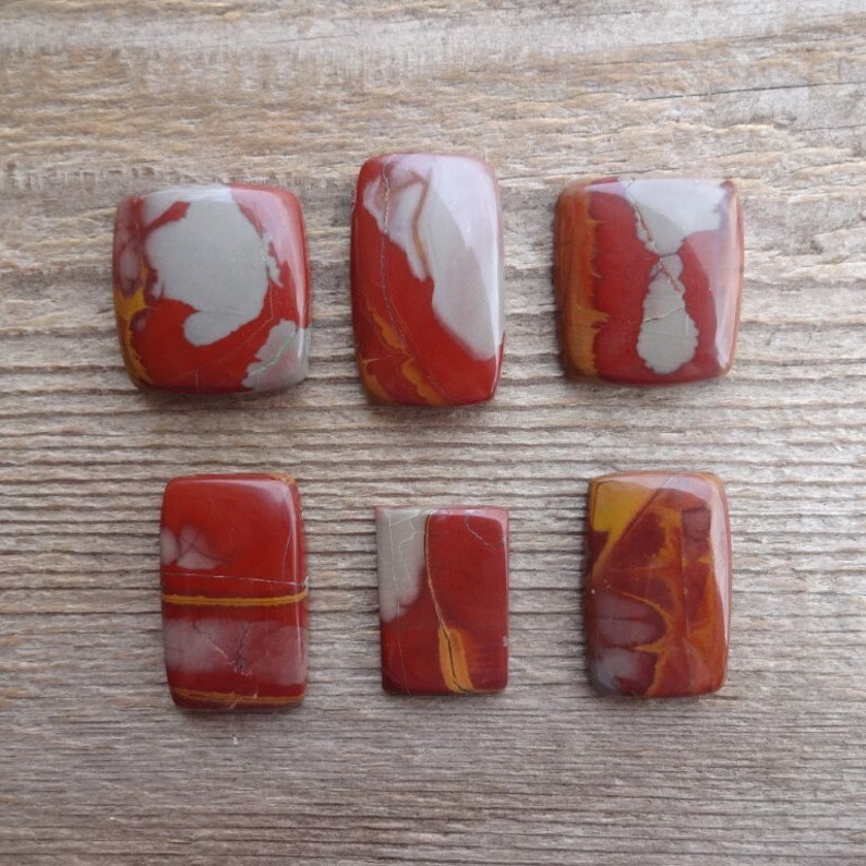 May include: Six red, white, and yellow jasper cabochons, each with a unique pattern. The cabochons are rectangular and have a smooth, polished surface.