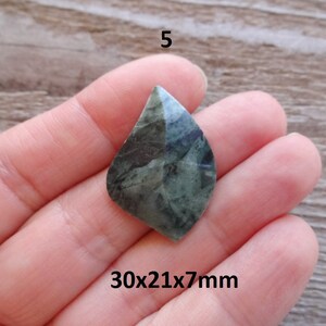 Puede incluir: Un colgante de piedra preciosa verde y negra en forma de l&aacute;grima, que mide 30x21x7mm. El colgante se sostiene en una mano.