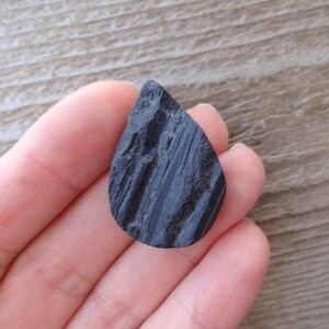 May include: A black teardrop-shaped stone with a rough, textured surface.