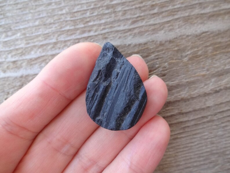 May include: A black teardrop-shaped stone with a rough, textured surface.