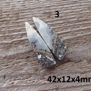 Puede incluir: Dos colgantes de piedra pulida con un patr&oacute;n gris, blanco y negro, y un toque de naranja. Los colgantes tienen forma de tri&aacute;ngulos alargados. El texto "3" est&aacute; encima de los colgantes y "42x12x4mm" debajo. Se muestran sobre una superficie de madera.
