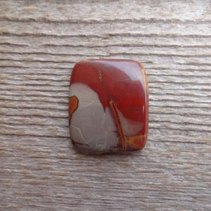 May include: A red, white, and orange cabochon gemstone with a unique pattern. The gemstone is rectangular and has a smooth, polished surface.