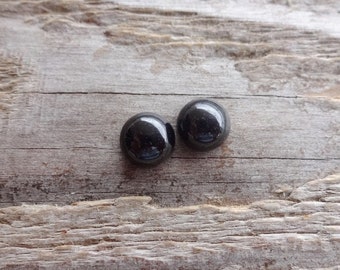 Pode incluir: Dois cabochões redondos de vidro preto sobre uma superfície de madeira.
