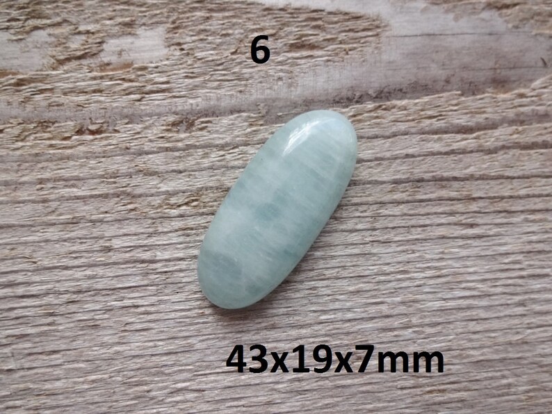 K&ouml;nnte beinhalten: Ein hellblauer ovaler Cabochon-Edelstein mit den Ma&szlig;en 43x19x7mm. Der Stein hat eine glatte, polierte Oberfl&auml;che und ein subtiles, wolkiges Muster.