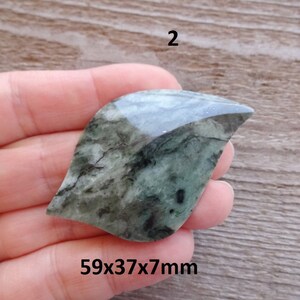 Puede incluir: Una piedra verde y negra con forma de hoja con una superficie lisa y pulida. La piedra mide 59x37x7mm.