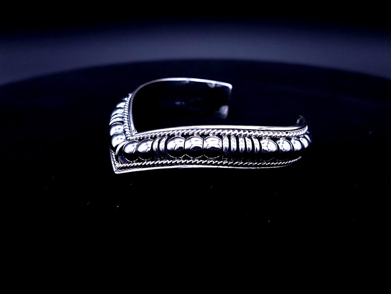 May include: A silver cuff bracelet with a V-shaped design. The bracelet features a row of small, round beads and a twisted rope-like pattern along the edges. The open cuff design allows for easy wear.