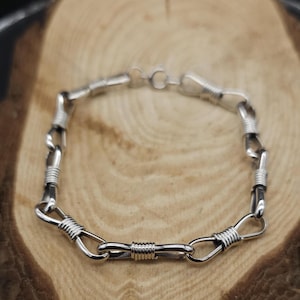 May include: A silver bracelet with a unique, twisted wire design. The bracelet is made of multiple interconnected loops, creating a textured and intricate look.
