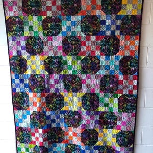 May include: A colorful quilt with a patchwork design. The quilt features a grid pattern of squares in various colors, including red, blue, green, and yellow. Interspersed within the squares are larger, octagonal shapes with a dark, patterned design. The quilt is bordered with a black fabric.