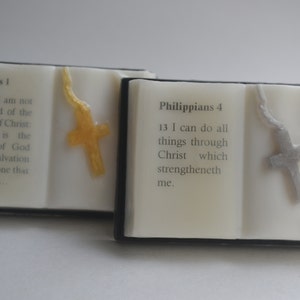 May include: Two small, white, book-shaped soaps with black borders. Each soap has a cross on the front, one is gold and the other is silver. The text on the front of the soaps reads "Romans 1" and "Philippians 4".