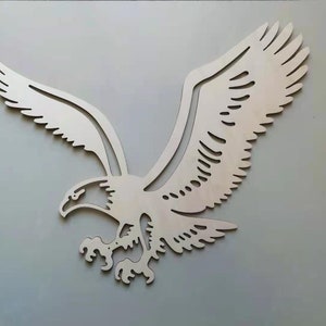 May include: A wooden cutout of an eagle in flight. The eagle is facing left and has its wings spread wide. The cutout is a light brown color and has a smooth finish.