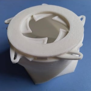 Könnte beinhalten: Ein weißes, 3D-gedrucktes Objekt mit einem kreisförmigen Oberteil und einem geometrischen Design. Der obere Ring hat eine strukturierte Oberfläche und umgibt eine Öffnung mit gebogenen, dreieckigen Elementen. Die Basis hat eine verdrehte, eckige Form.