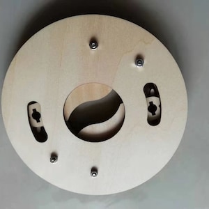 May include: A round wooden base with a cutout in the center, designed for a circular object. The base has four screw holes and two slots on the sides. The wood is a light brown color.