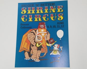 Könnte beinhalten: Ein Vintage-Plakat, das für den Shrine Circus in Denver, Colorado wirbt. Das Plakat zeigt eine farbenfrohe Illustration eines Elefanten, der einen roten Fez trägt, und eines Clowns, der ein Buch hält. Der Text auf dem Plakat lautet "Bigger 'N' Better! Shrine Circus" und "June 8, 9, 10, 11, and 12, 1973".