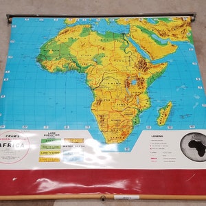 May include: A vintage, rolled-up map of Africa with a blue ocean, green and brown land masses, and a legend and scale. The map is titled "Cram's Physical-Political Africa".