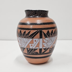 May include: A small, brown ceramic vase with black and white geometric designs. The vase has a rounded body and a narrow opening.