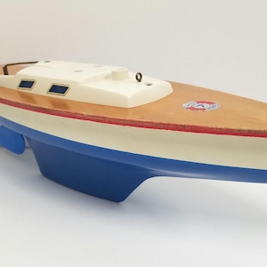 May include: A wooden toy sailboat with a blue hull, white deck, and red trim. The sailboat has a small cabin and a mast.