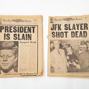 May include: Two vintage newspaper front pages with headlines about the assassination of President John F. Kennedy. The left page reads "President Is Slain" and the right page reads "JFK Slayer Shot Dead".