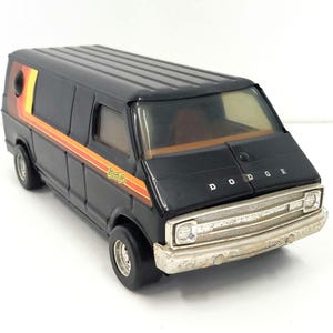 May include: Black toy Dodge van with orange and yellow stripes and the word "Smile" on the side. The van has a silver grill and headlights.