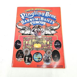 May include: A red and white program for the 100th anniversary of Ringling Bros. and Barnum & Bailey Circus. The cover features a tiger with an open mouth, two elephants, and a circus wagon. The text "The Greatest Show on Earth" is visible in a circle.