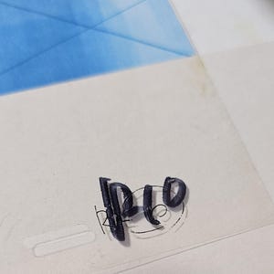 May include: A clear animation cel featuring a vibrant blue painted section at the top. The bottom portion is transparent and displays the black ink text "RP10" written in a stylized, hand-drawn font with a circular outline around the letters.