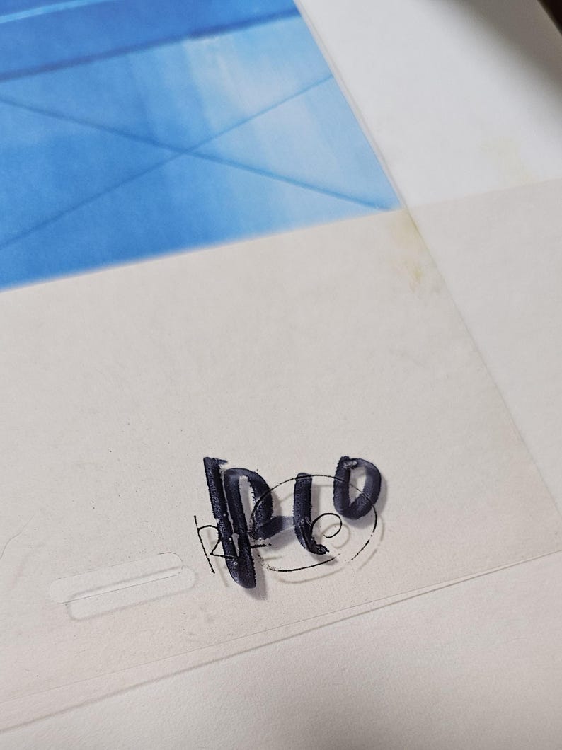 May include: A clear animation cel featuring a vibrant blue painted section at the top. The bottom portion is transparent and displays the black ink text "RP10" written in a stylized, hand-drawn font with a circular outline around the letters.