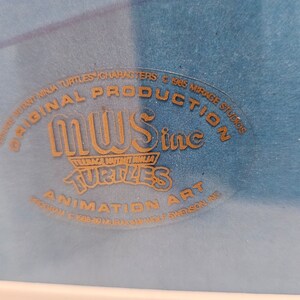 May include: A blue animation art cel featuring a gold embossed seal that reads ORIGINAL PRODUCTION MWS inc TEENAGE MUTANT NINJA TURTLES ANIMATION ART, with additional text including 1985 MIRAGE STUDIOS and 1988-89 MURAKAMI WOLF SWENSON INC.