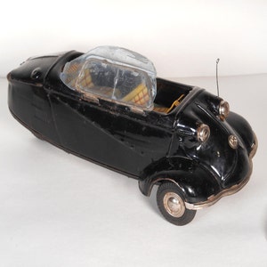 May include: Black toy car with a clear plastic roof and a yellow interior. The car has a chrome bumper and headlights.
