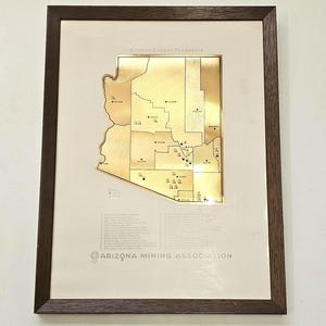May include: Framed artwork featuring a gold-colored map of Arizona, highlighting copper producers. The map is set against a cream-colored background, with text at the top and bottom. The frame is dark brown.