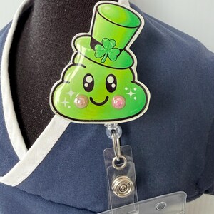 Op de afbeelding: Een groene badge reel met St. Patrick's Day-thema met een cartoon poep-emoji met een groene hoge hoed met een klavertje vier. De badge reel heeft een doorzichtige plastic ID-houder en een intrekbaar koord.