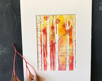 May include: A matted watercolor print featuring white birch trees against a vibrant yellow and orange autumn forest background. The text reads: I'M SO GLAD I LIVE IN A WORLD WHERE THERE ARE OCTOBERS. Anne of Green Gables L.M. Montgomery.