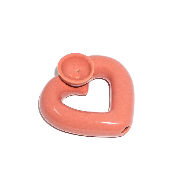 May include: A pink ceramic heart-shaped pipe with a round bowl on top.