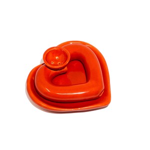 May include: Orange ceramic heart-shaped incense burner with a small round hole in the center. The burner is made of two pieces, a heart-shaped base and a smaller heart-shaped top.