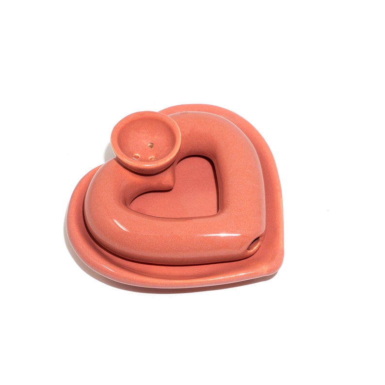 May include: A pink ceramic heart-shaped incense burner with a small bowl on top. The bowl has three holes in it.