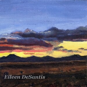 May include: A painting of a sunset over a mountain range. The sky is a vibrant blue with streaks of pink, orange, and yellow. The mountains are dark and silhouetted against the sky. The artist's signature, Eileen DeSantis, is visible in the bottom left corner.