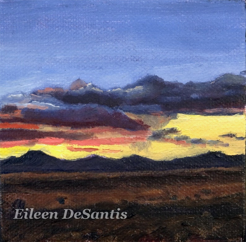 May include: A painting of a sunset over a mountain range. The sky is a vibrant blue with streaks of pink, orange, and yellow. The mountains are dark and silhouetted against the sky. The artist's signature, Eileen DeSantis, is visible in the bottom left corner.
