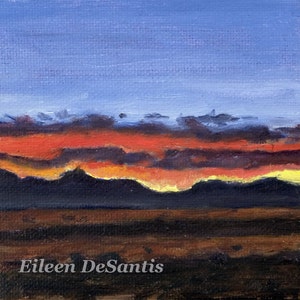 May include: A painting of a sunset over a mountain range. The sky is a deep blue with streaks of orange, red, and yellow. The mountains are silhouetted against the sky. The artist's signature, Eileen DeSantis, is in the bottom right corner.