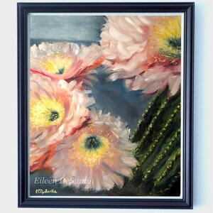 May include: Oil painting of cactus flowers in pink, yellow, and green hues. The artwork is framed in a dark blue frame and signed by the artist, Eileen DeSantis. The painting is a close-up of the flowers.
