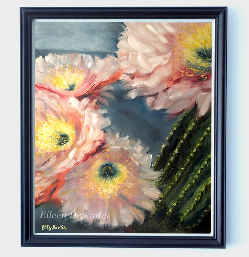 May include: Oil painting of cactus flowers in pink, yellow, and green hues. The artwork is framed in a dark blue frame and signed by the artist, Eileen DeSantis. The painting is a close-up of the flowers.