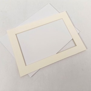 May include: A rectangular, off-white picture mat with a white backing, ideal for framing artwork or photographs. The mat has a clean, simple design with a rectangular opening, and is set against a white background.
