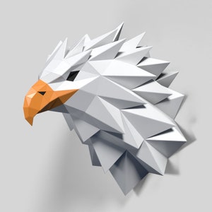 Puede incluir: Escultura de cabeza de águila de papel blanco con un pico naranja. La escultura está hecha de papel doblado y tiene un diseño geométrico.