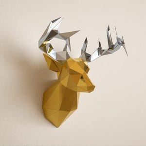 Peut inclure: Une sculpture murale géométrique représentant une tête de cerf avec une finition dorée sur le cou et le visage, contrastée par des bois métalliques argentés très réfléchissants, formés de facettes angulaires créant un aspect moderne.