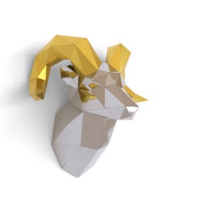 May include: A geometric wall-mounted ram head sculpture. The ram's horns are gold, and the head is silver. The sculpture is made of angular, faceted shapes, creating a modern, artistic look. The artwork is set against a white background.