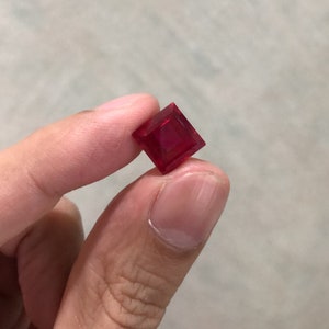 May include: A deep red square-shaped gemstone with a faceted cut.