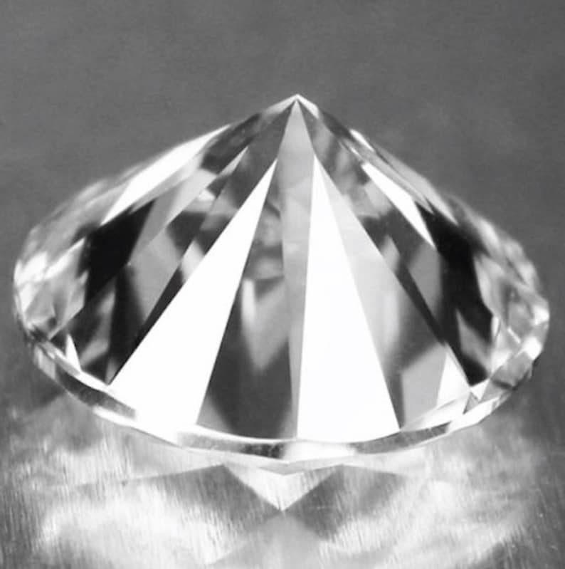 May include: A clear, round, faceted diamond with a pointed top.