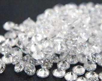 May include: A pile of loose, clear, faceted, round diamonds. The diamonds are scattered on a black surface.