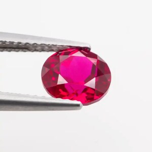 May include: A vibrant red ruby gemstone held in tweezers. The ruby is round and faceted, showcasing its brilliance.
