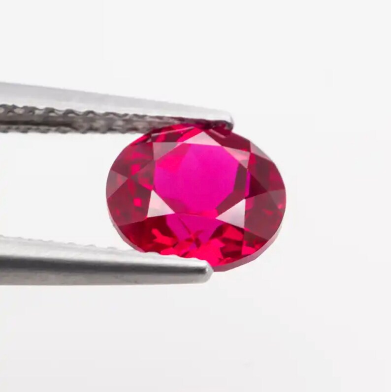 May include: A vibrant red ruby gemstone held in tweezers. The ruby is round and faceted, showcasing its brilliance.