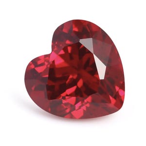 May include: A deep red heart-shaped gemstone with a faceted cut. The gemstone is set against a white background.