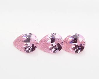 May include: Three pear-shaped pink gemstones on a white background.